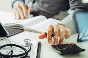 Medical Billing Outsourcing: What Should You Look For? | Man working at desk with calculator and stethoscope